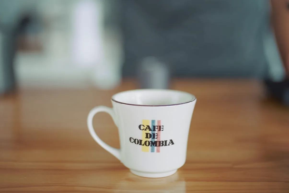 木のカウンターに置かれた、CAFE DE COLOMBIA のカップ